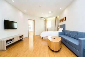 A modern hotel room with a bed, a blue sofa, a wooden coffee table, a TV, and a painting on the wall. - HanTing Hotel (Tianjin Hospital Jiefang South Road) (Tianjin)