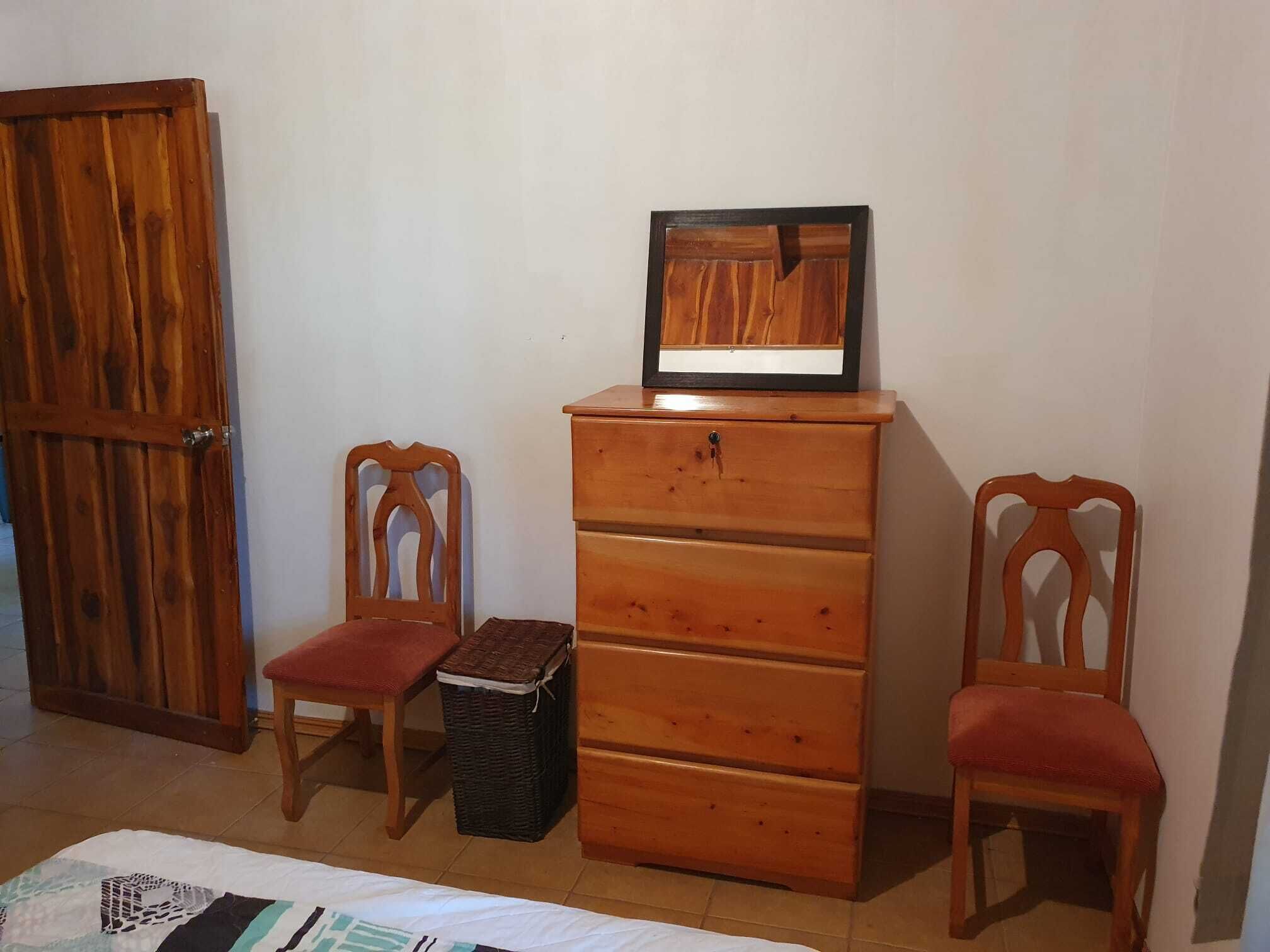Quarto com guarda-roupa de madeira, duas cadeiras de madeira, uma cesta de vime e uma cama.