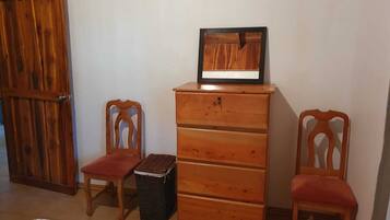 Quarto com guarda-roupa de madeira, duas cadeiras de madeira, uma cesta de vime e uma cama.