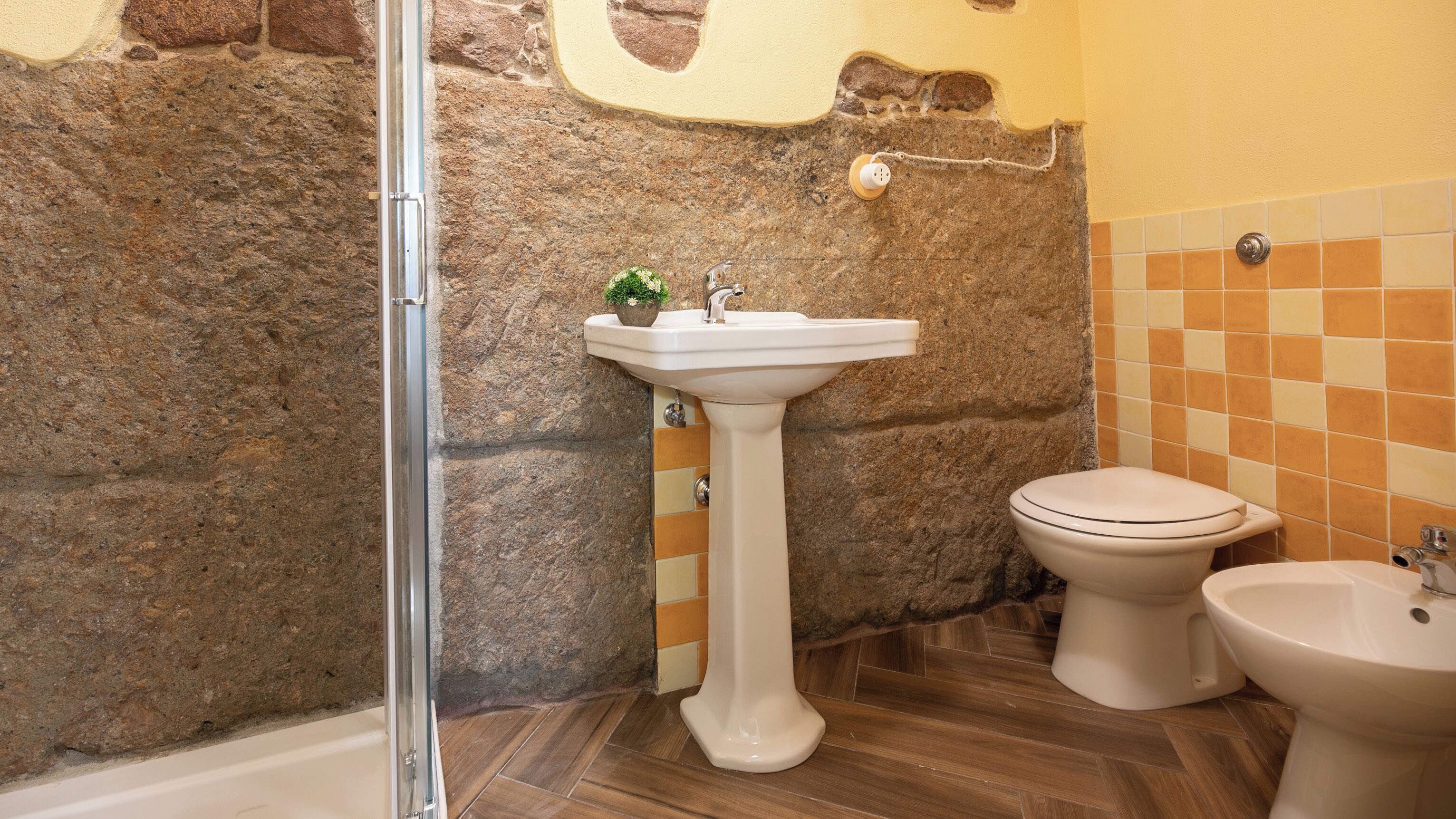 Ein Badezimmer mit Steinwand, einem weißen Waschtisch, einer Toilette und einem Bidet.