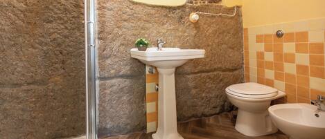 Ein Badezimmer mit Steinwand, einem weißen Waschtisch, einer Toilette und einem Bidet.
