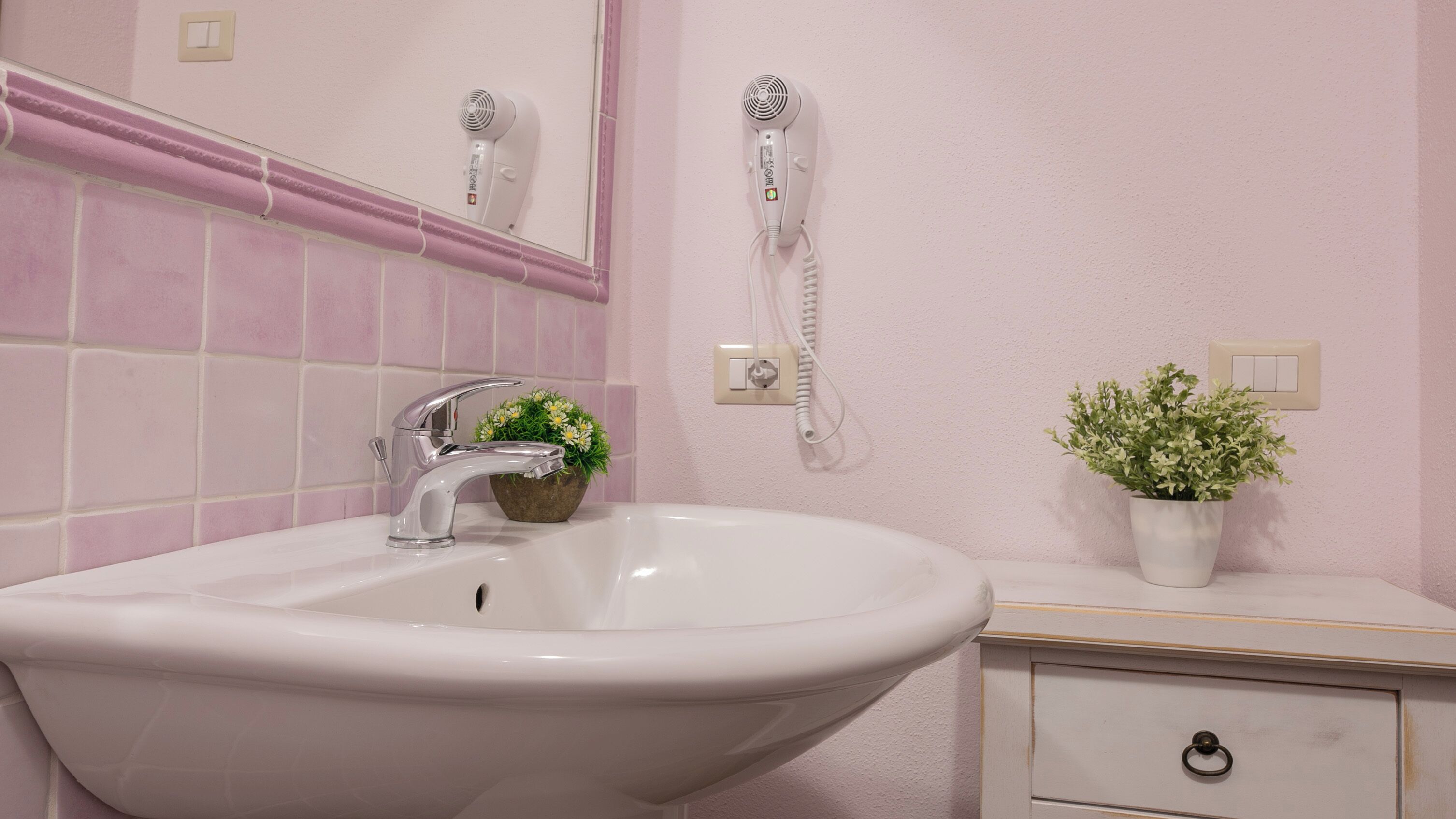 Un bagno con lavandino bianco, uno specchio, un asciugacapelli, un telefono e una piccola pianta in vaso.