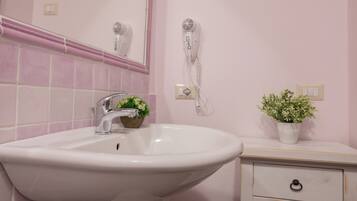 Un bagno con lavandino bianco, uno specchio, un asciugacapelli, un telefono e una piccola pianta in vaso.