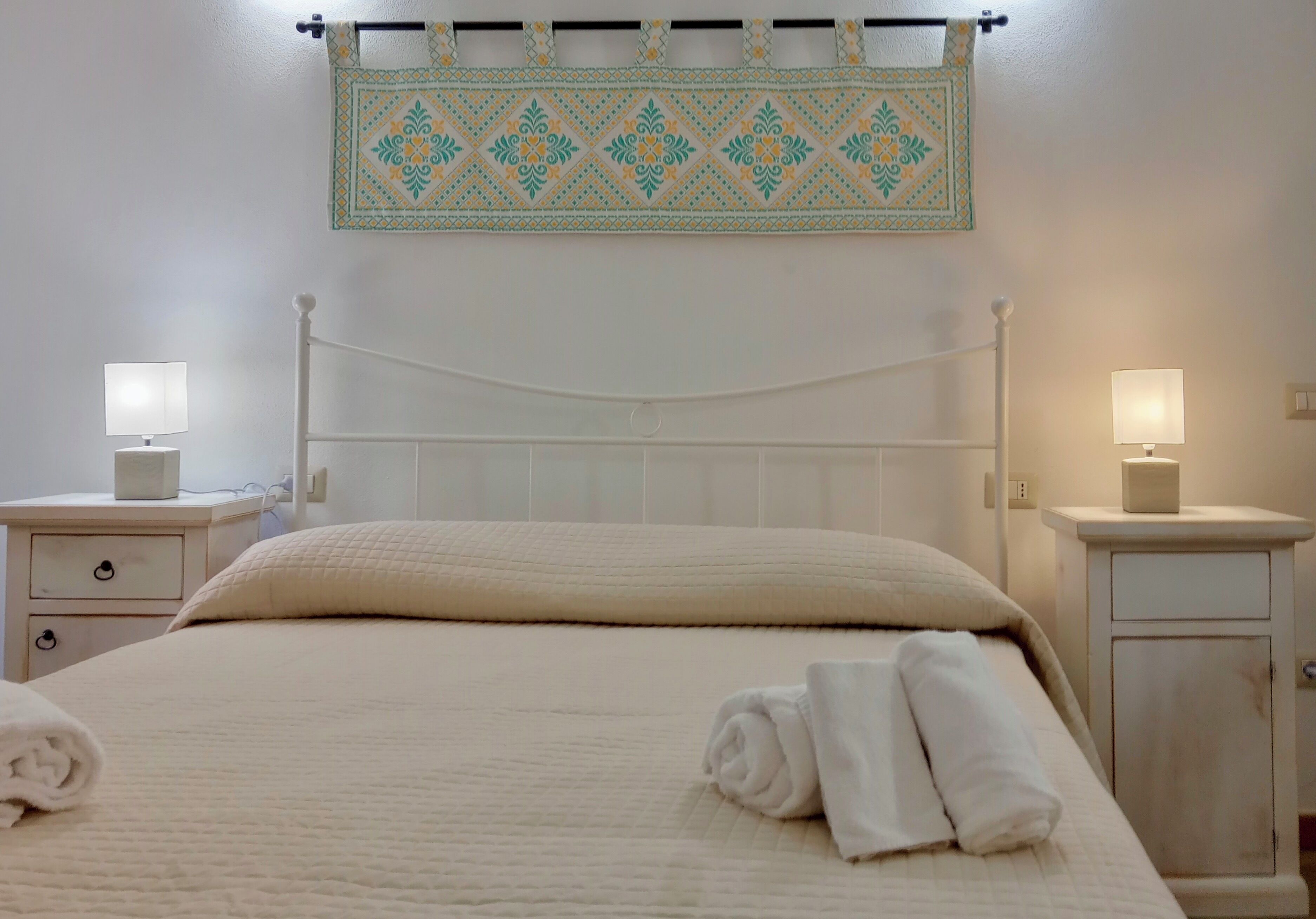 A neatly made bed with a quilt, two bedside tables with lamps, and a decorative wall hanging above.