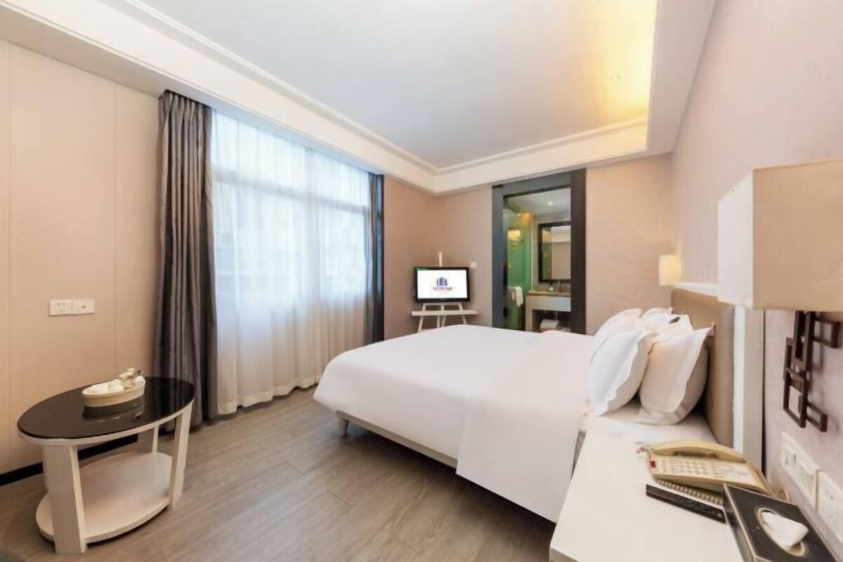 A hotel room with a bed, a desk with a telephone, a small table, a TV, and a mirror.