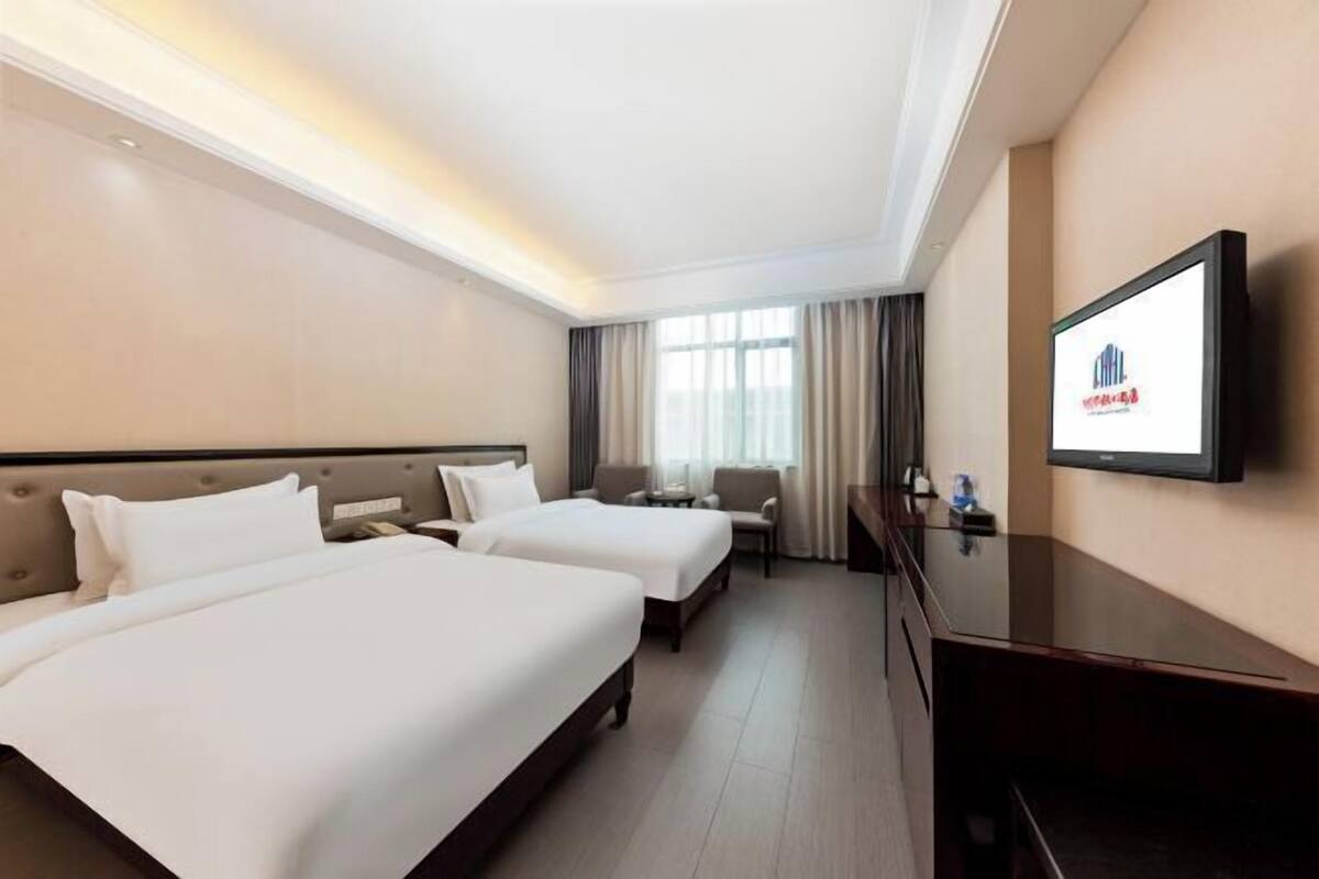 A hotel room with two beds, a TV, a desk, and a window with curtains.