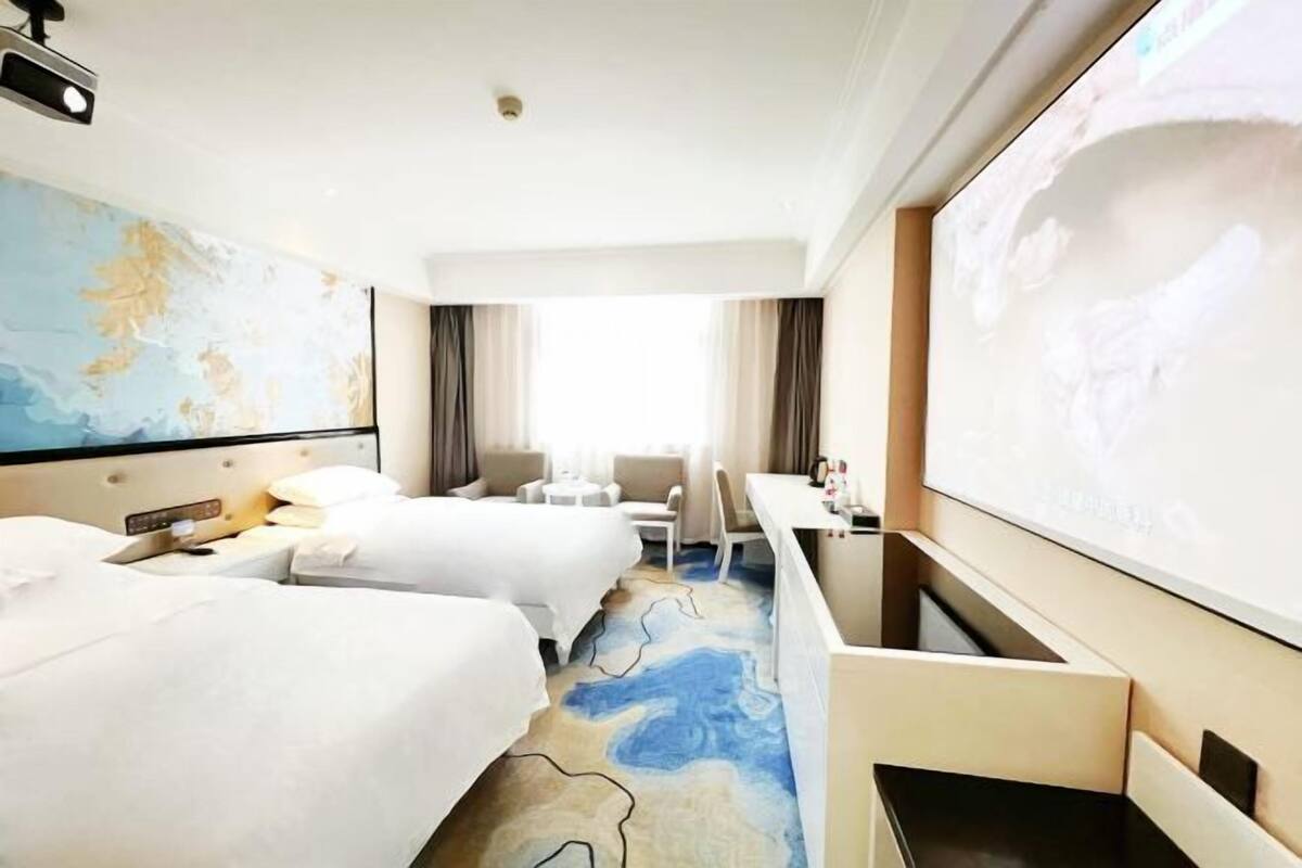 A hotel room with two beds, a desk, a chair, a map on the wall, and a large screen.