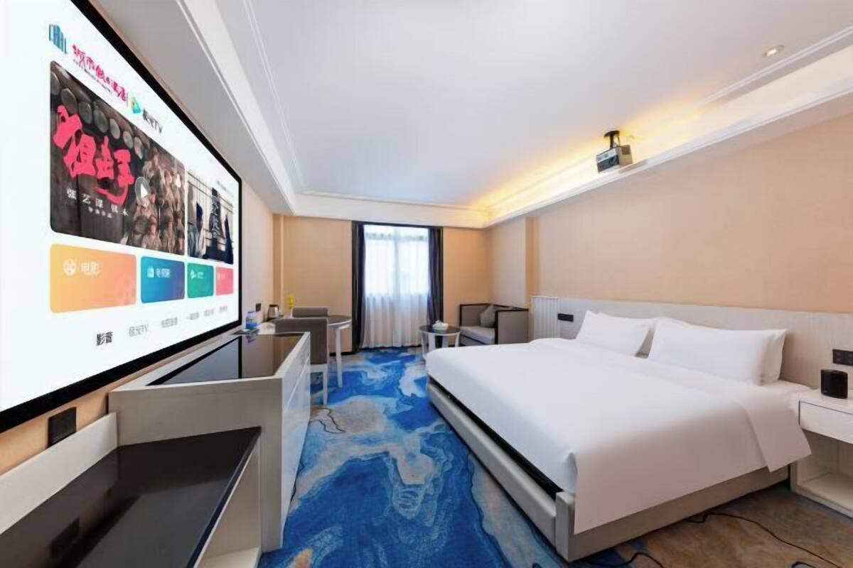 A hotel room with a bed, a desk, a chair, a TV, and a window with curtains.