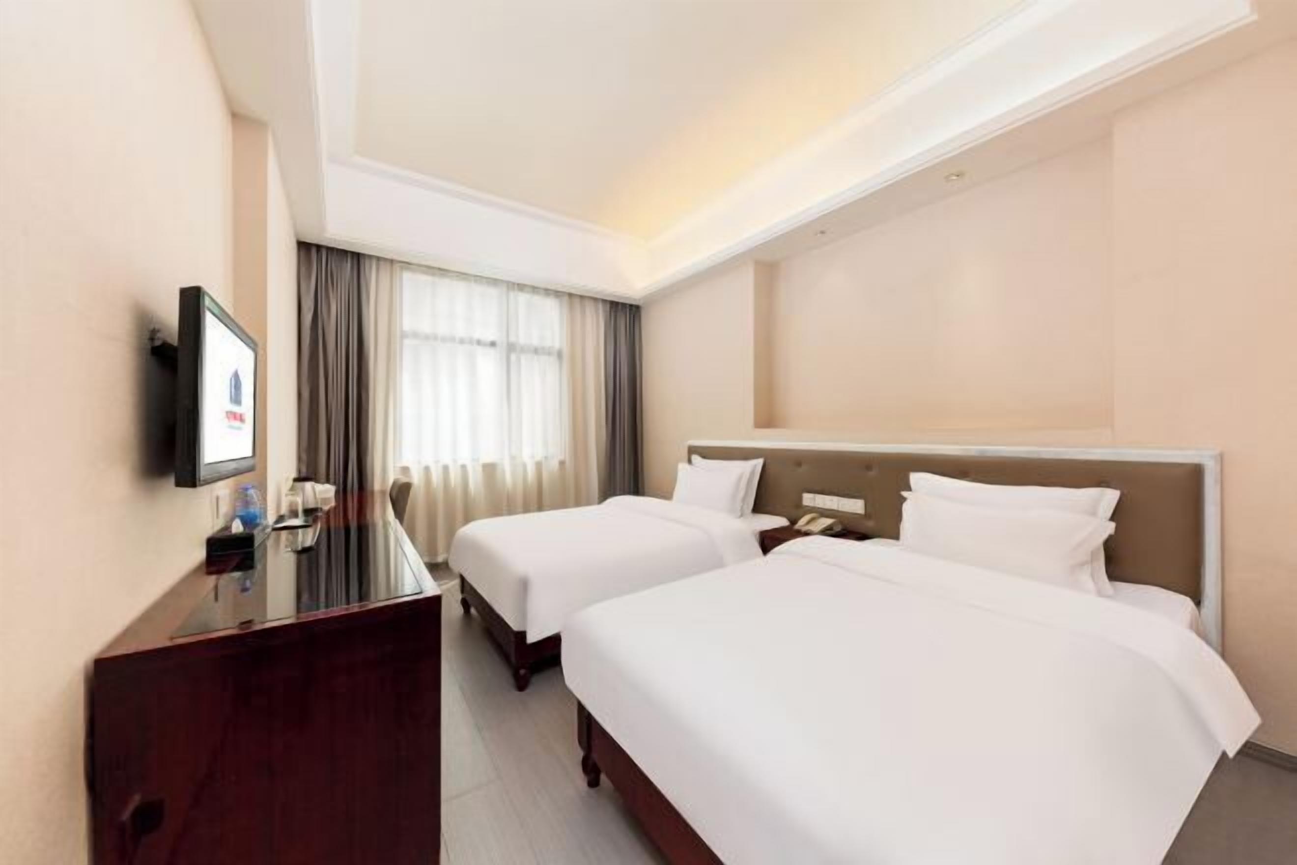 A hotel room with two beds, a desk, a TV, and a window with curtains.