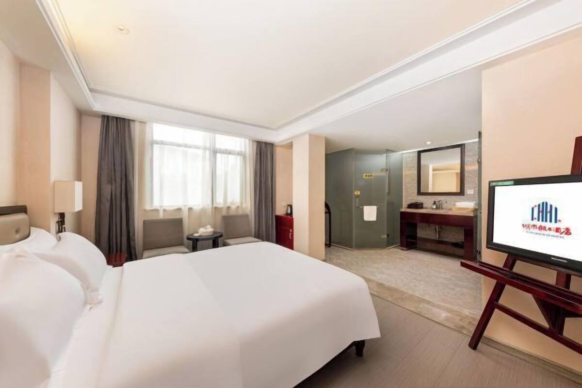 A hotel room with a large bed, a desk, a chair, a TV, a bathroom, and a shower.