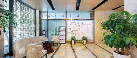 A lobby with a sofa, chairs, a reception desk, and a potted plant.