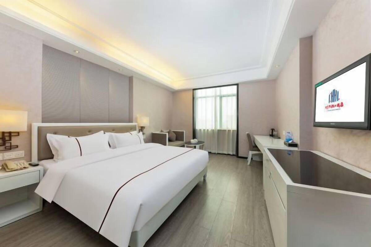 A hotel room with a bed, bedside table, desk, and a TV on the wall.