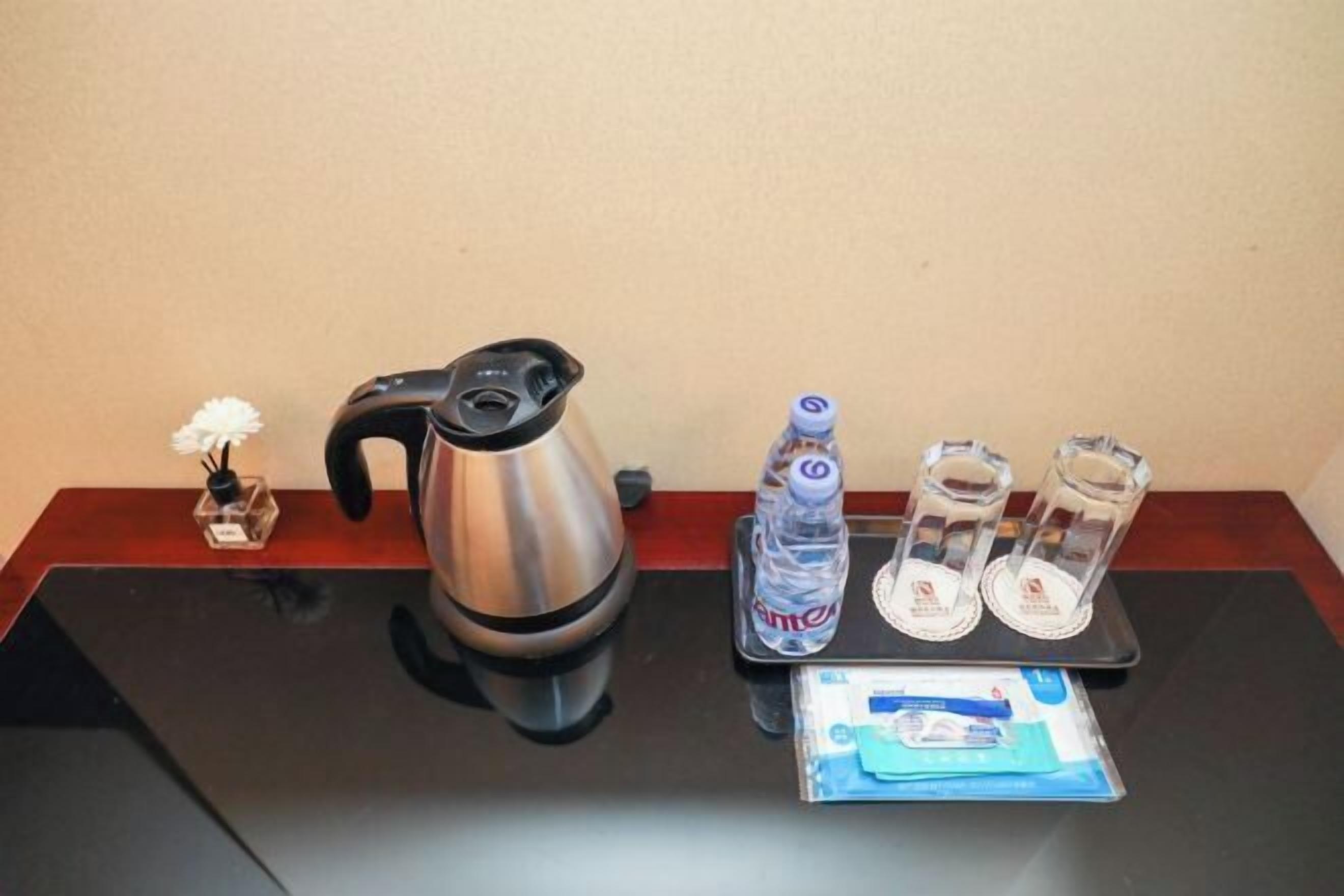 A table with a coffee maker, a water bottle, two glasses, and a packet of tissues.