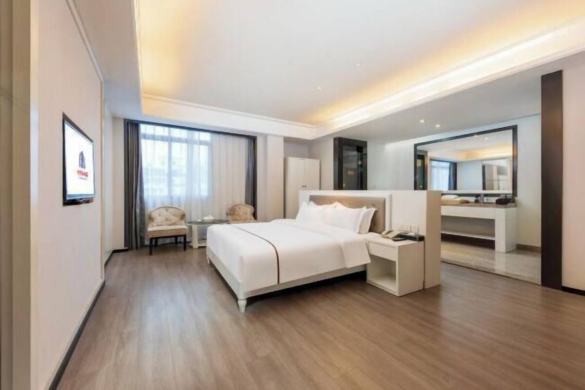 A modern hotel room with a bed, bedside table, chair, and a large mirror.
