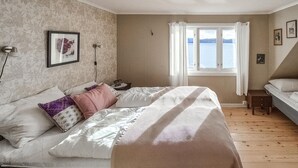 Un dormitorio con cama, ventana con cortinas, mesita de noche y lámpara de pared.