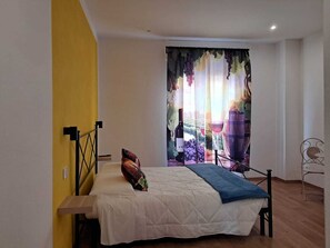 A bedroom with a bed, a nightstand, a window with a vineyard view, and a yellow wall. - B&B 8380 La Cantina di Piero e 'Netta (Manciano)