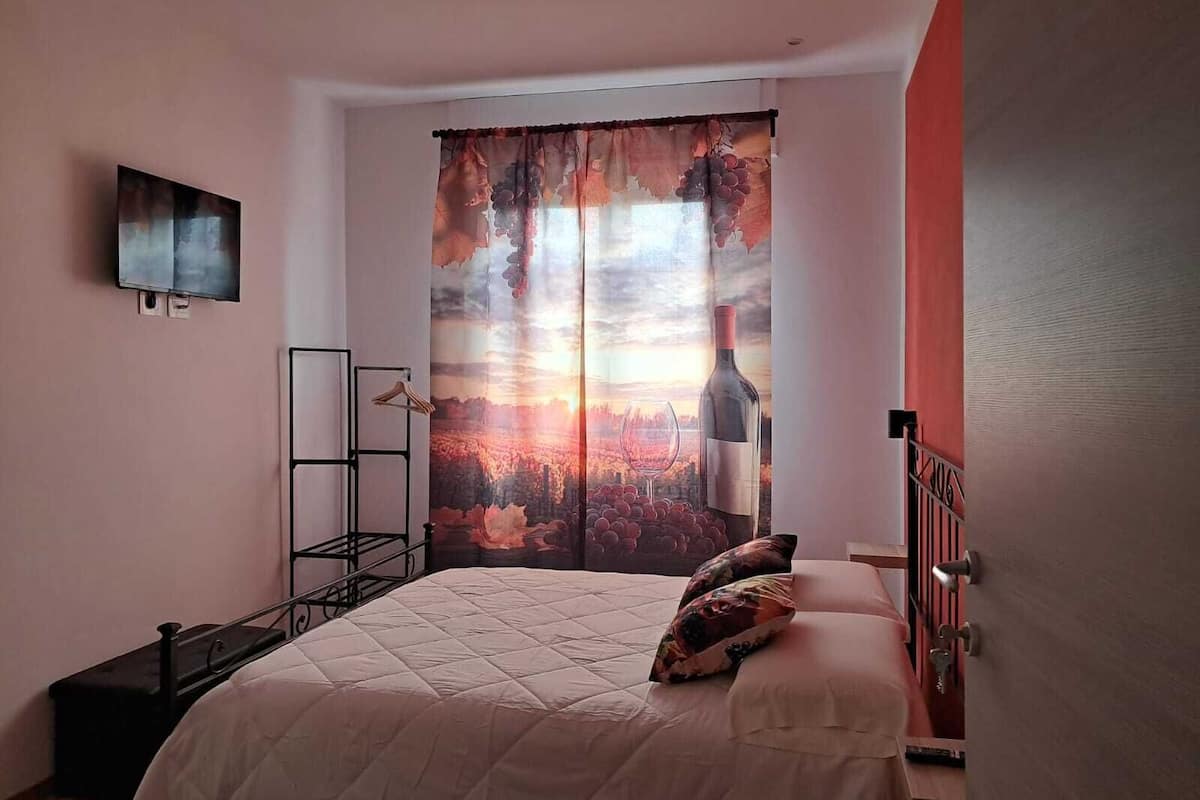 A bedroom with a bed, a wardrobe, a TV mounted on the wall, and a window with a sunset view.