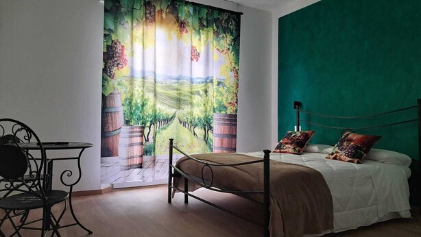 A bedroom with a bed, a chair, a table, and a large window with a vineyard curtain. - B&B 8380 La Cantina di Piero e 'Netta (Manciano)