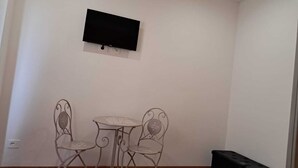 A small room with a flat-screen TV mounted on the wall, a small round table with two chairs, and a black speaker. - B&B 8380 La Cantina di Piero e 'Netta (Manciano)