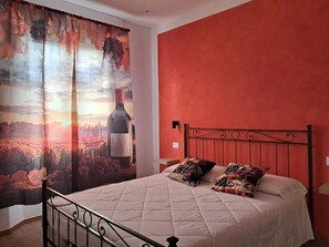 A bedroom with a bed, a red wall, and a curtain with a grapevine and sunset scene. - B&B 8380 La Cantina di Piero e 'Netta (Manciano)