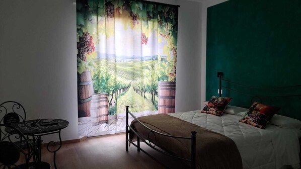 A bedroom with a bed, a table, and a view of a vineyard through a curtain. - B&B 8380 La Cantina di Piero e 'Netta (Manciano)