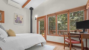 Een slaapkamer met een bed, een bureau en een stoel. Er is een raam met uitzicht op bomen en een balkon.