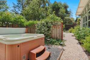 Ein Whirlpool in einem Garten mit Holzterrasse, umgeben von Bäumen und einem Kiesweg.