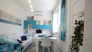 A modern living room with a white sofa, a dining table set with plates and glasses, and a TV mounted on the wall. - Galactic Sea: delightful cottage surrounded by greenery just minutes from the beach (Lido delle Nazioni)