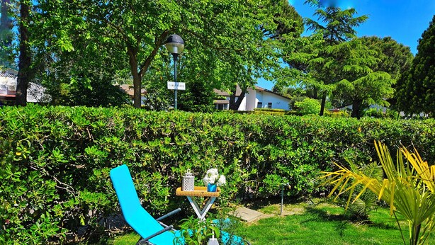 A well-maintained garden with a blue lounge chair, a small table with a lantern and flowers, and a potted plant. - Galactic Sea: delightful cottage surrounded by greenery just minutes from the beach (Lido delle Nazioni)