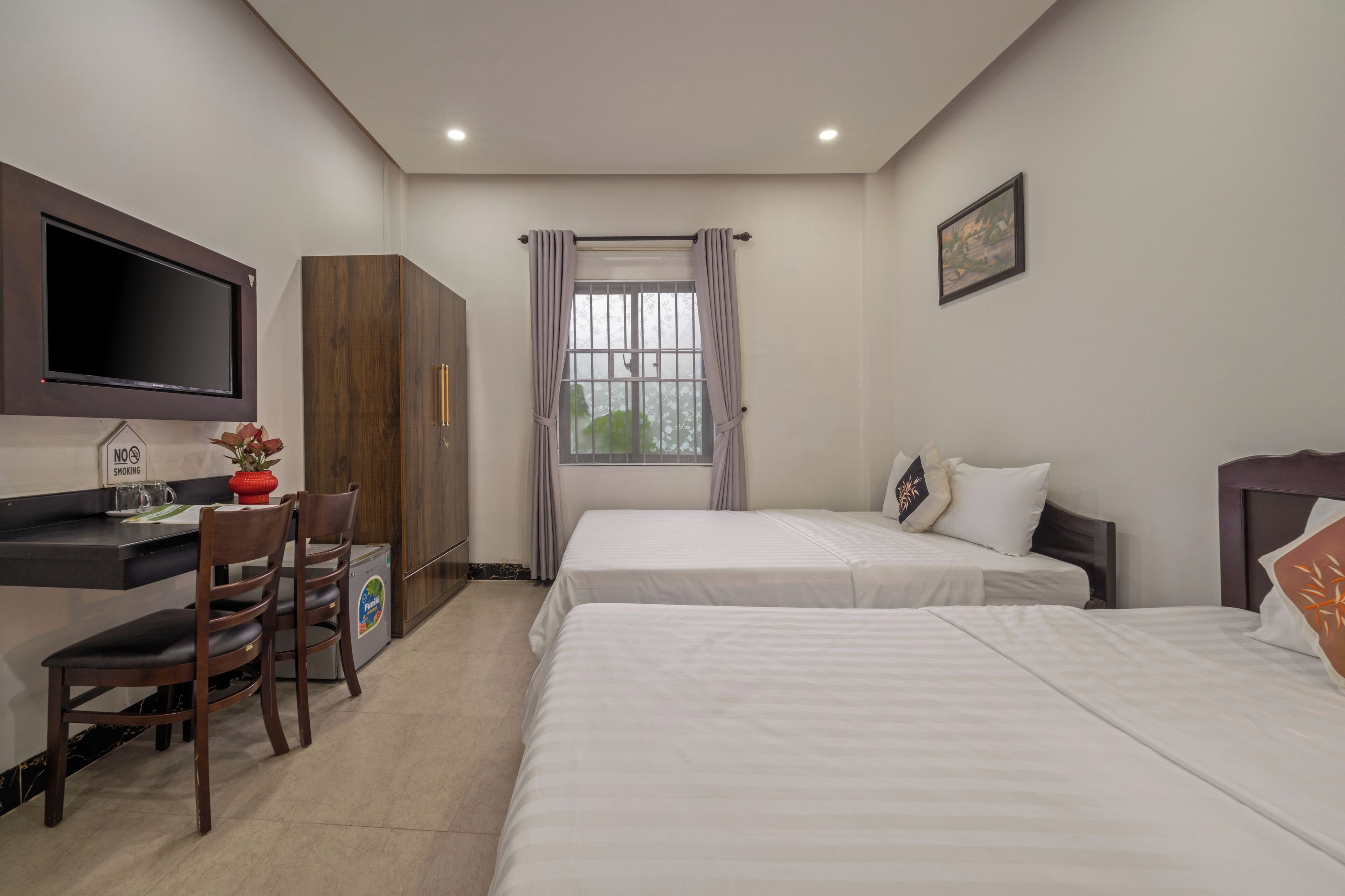Habitación de hotel con dos camas, un escritorio con silla, televisor montado en la pared y una ventana con cortinas.