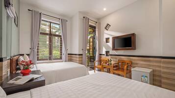 Habitación de hotel con dos camas, televisión, una mesita con una silla y ventana con cortinas.