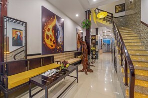 A modern lobby with a wooden bench, a reception desk, and a staircase with a stone wall. - Bo Bo Homestay Hoi An (Da Nang)