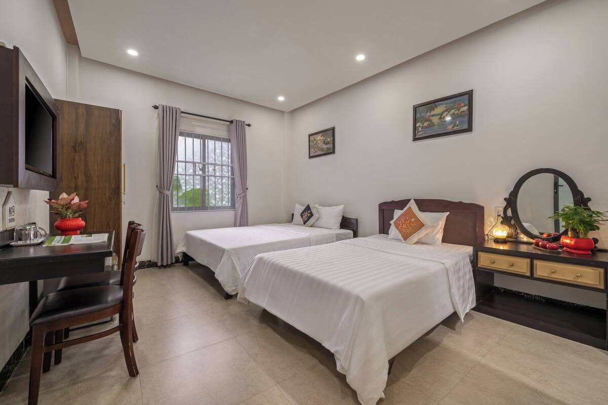 A hotel room with two beds, a desk with a chair, a TV, and a window with curtains.