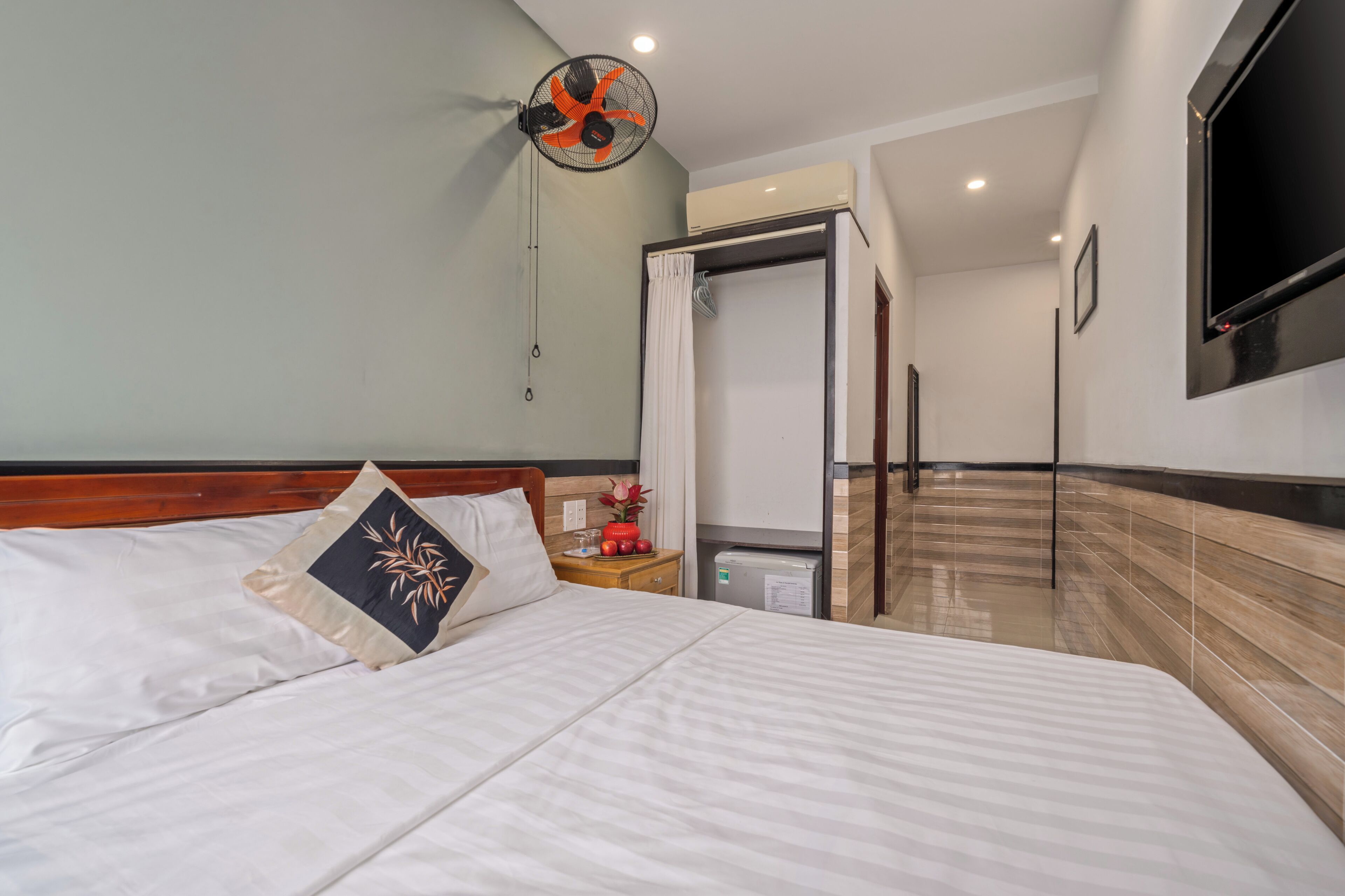 A hotel room with a bed, a nightstand, a fan, a TV, and a shower area.