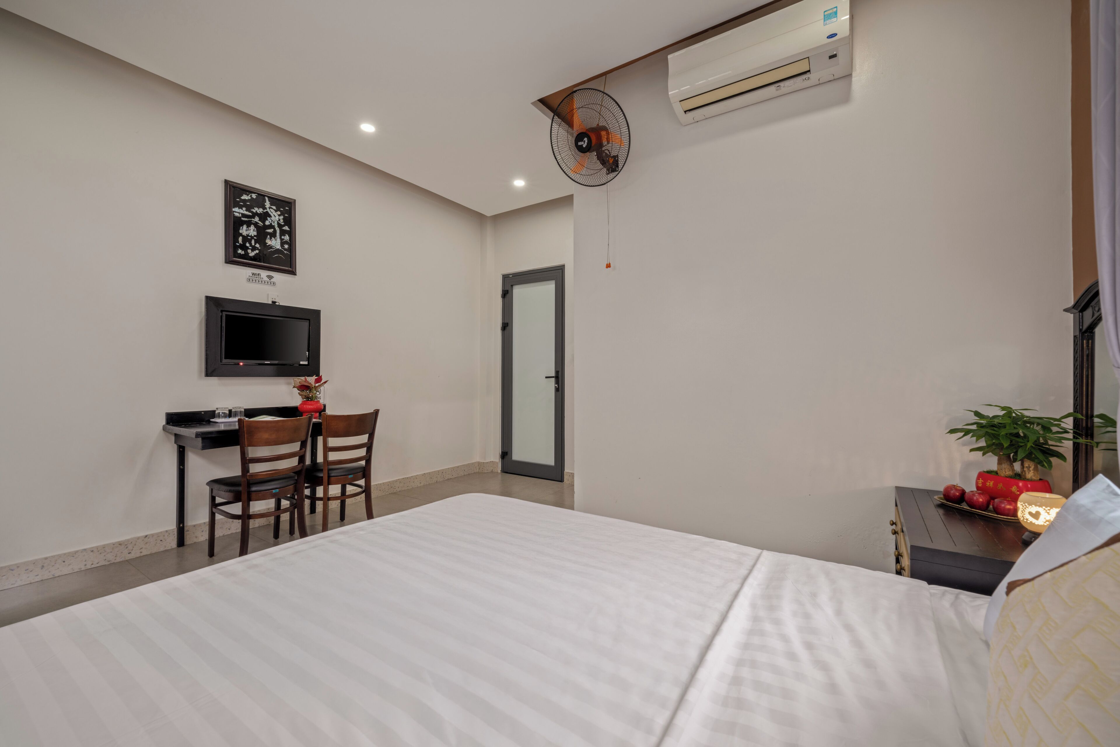 A hotel room with a bed, a desk with a chair, a television, an air conditioner, and a door.