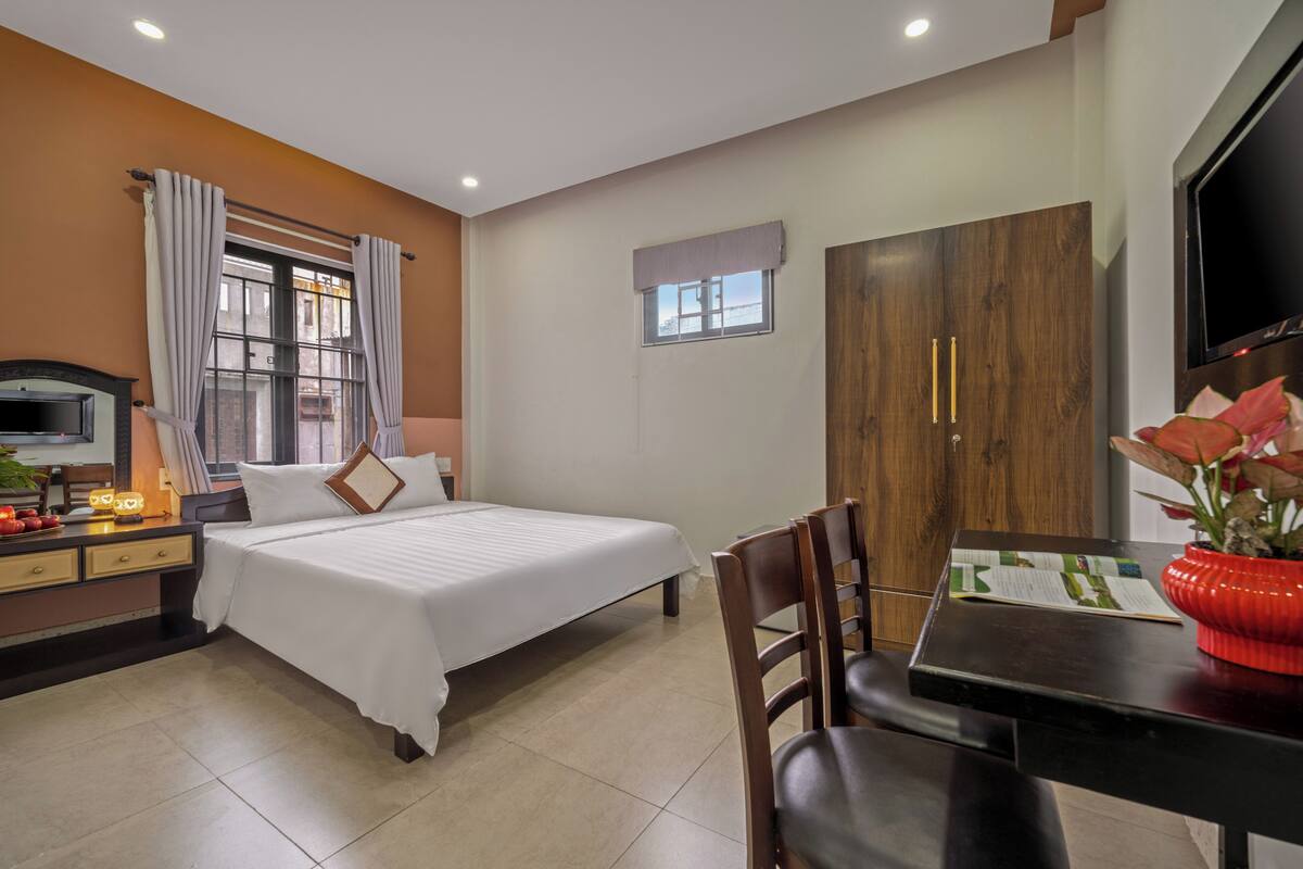 A hotel room with a bed, a desk with a chair, a TV, and a window with curtains.