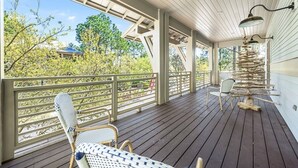 A covered outdoor deck with wooden flooring, metal railings, and wicker furniture. - Step into the blue, stay in the moment at Azure / Golf Cart / 4 Bikes (Santa Rosa Beach)