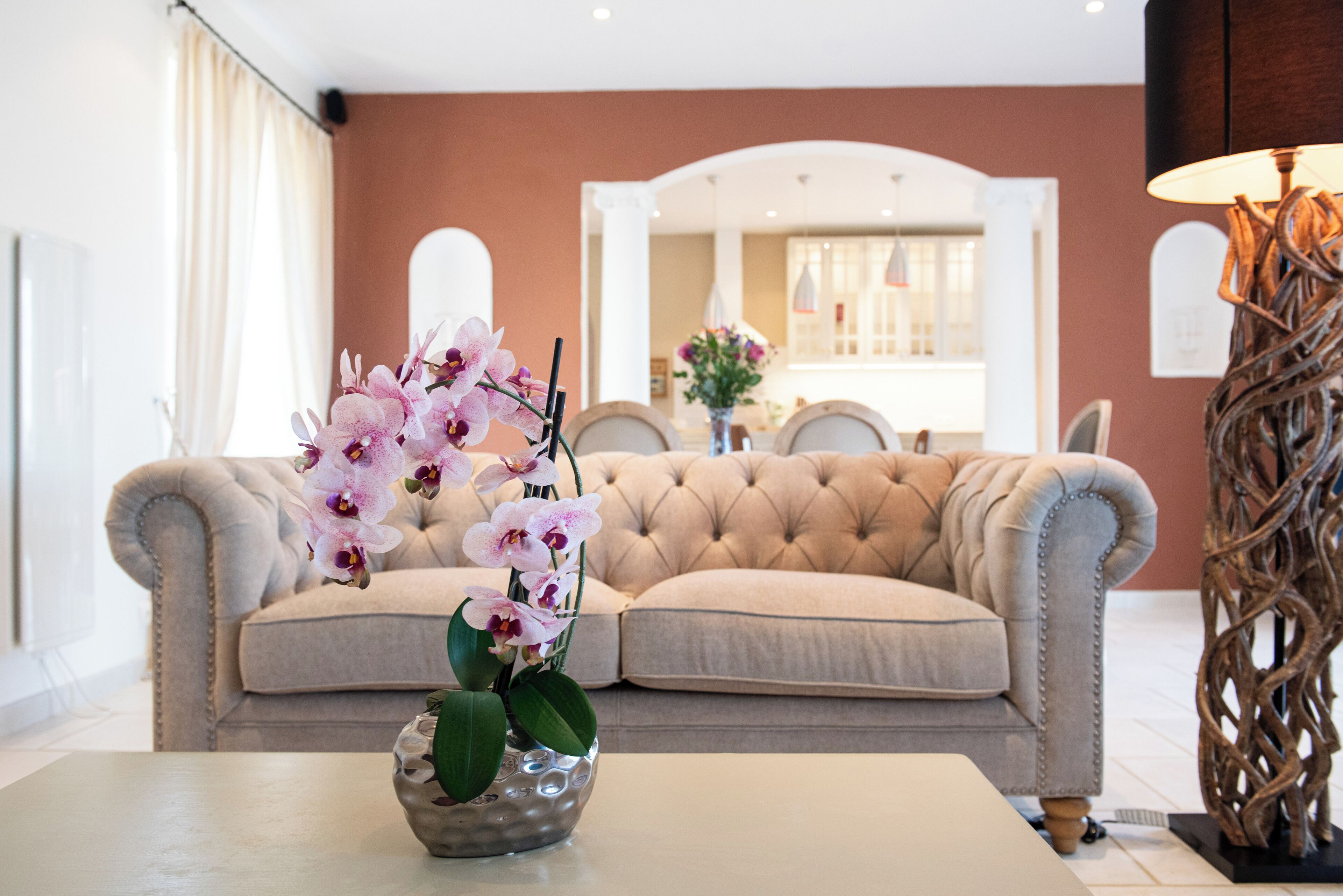 A living room with a beige sofa, a glass coffee table, and a vase of pink orchids.