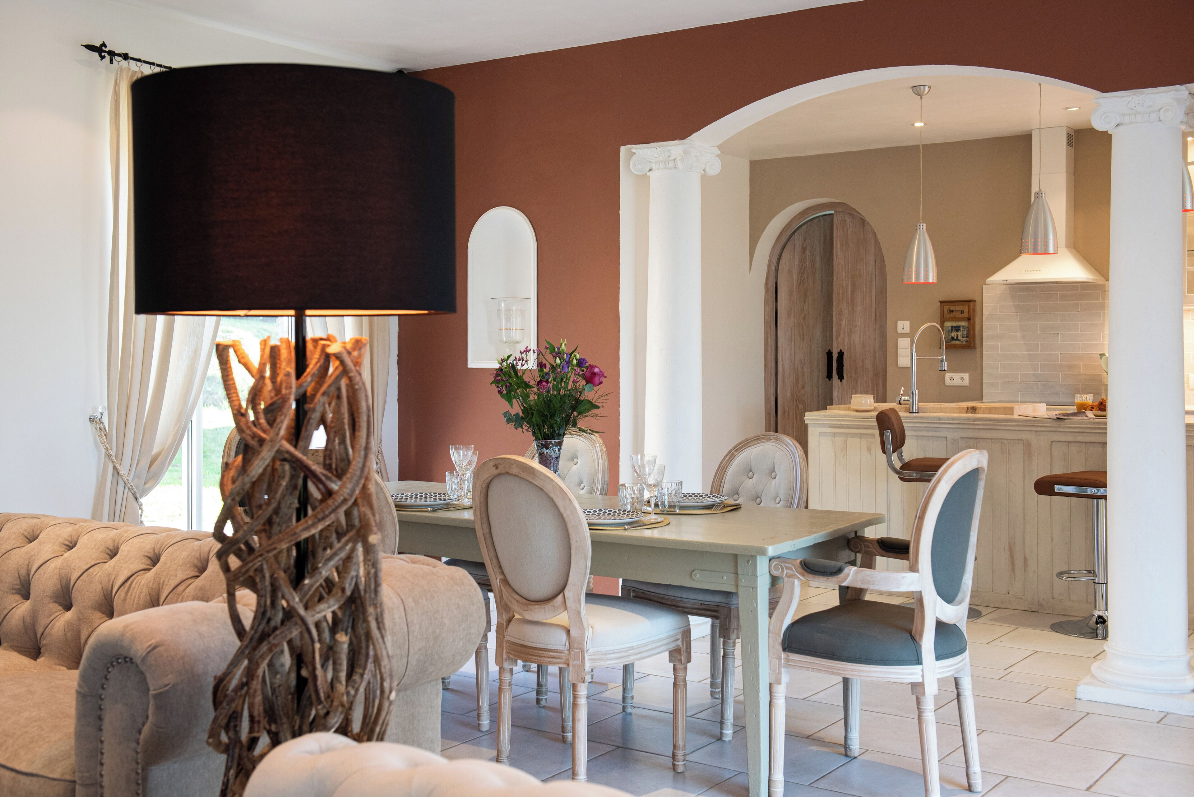 A dining area with a table set for four, surrounded by upholstered chairs. A large, dark-colored lamp hangs above the table.