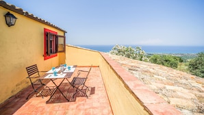 Een terras met een tafel en stoelen, een rood luik en uitzicht op zee.