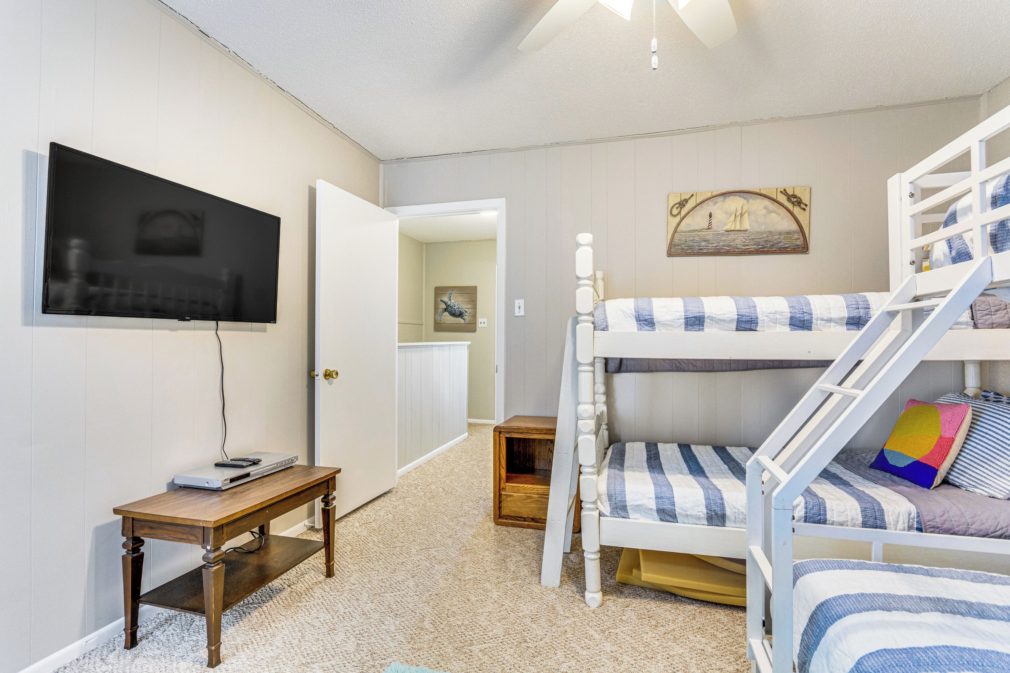 Une chambre avec des lits superposés, une télévision, une petite table en bois et une porte donnant sur une autre pièce.