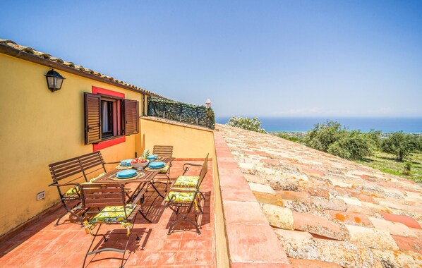 An outdoor dining area with a table and chairs, a bench, and a view of the sea. - Beautiful apartment in Collesano (PA) (Collesano (PA))
