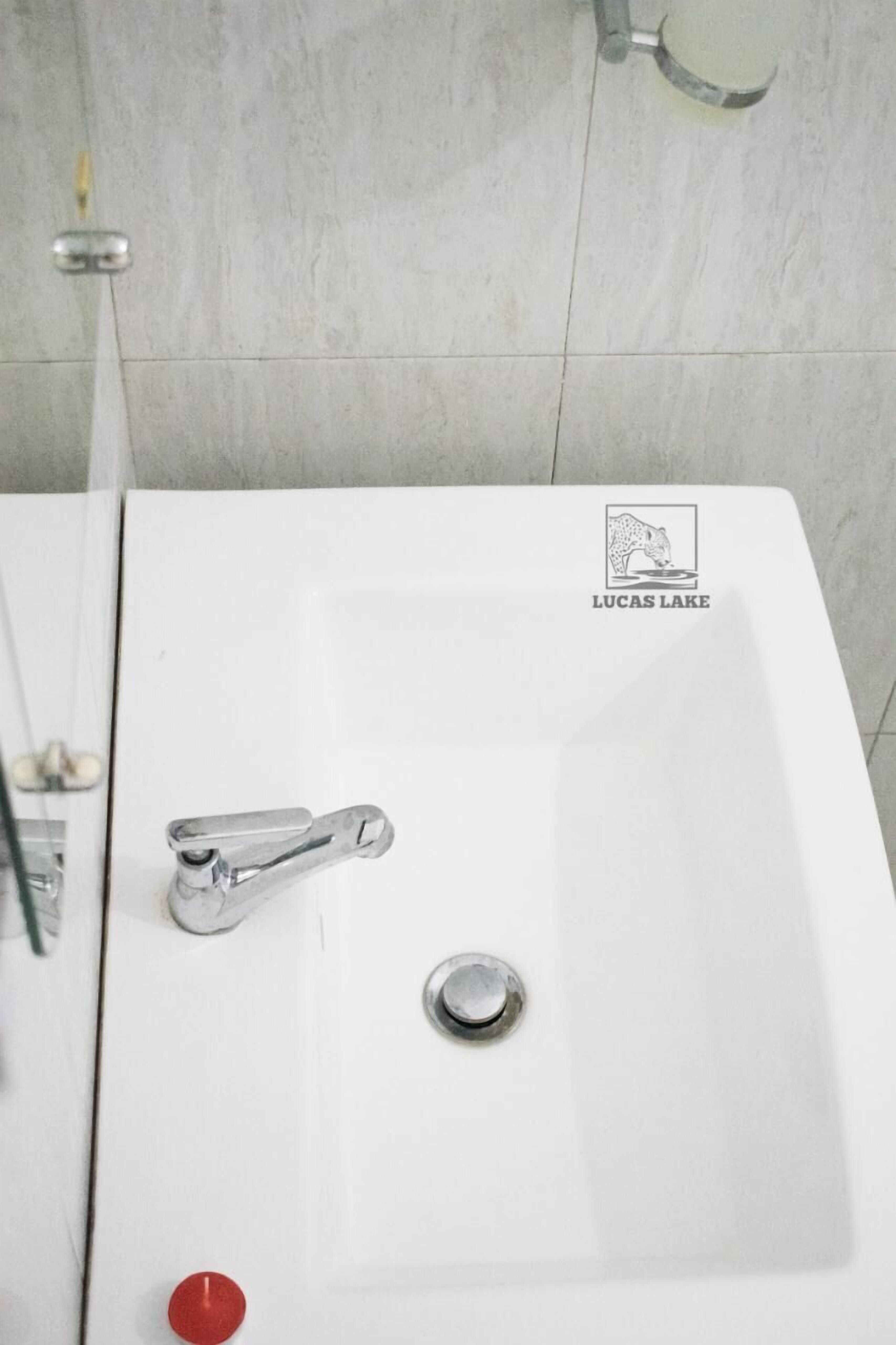 A white bathroom sink with a faucet and a red button, and a logo that reads "Lucas Lake".