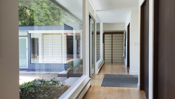 Un couloir moderne avec un plancher en bois, de grandes fenêtres et une vue sur un immeuble doté d’un garage.
