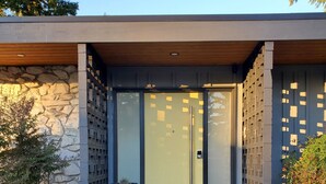 Une entrée moderne, avec une façade en pierre, une porte en verre et un petit escalier menant à l’entrée.
