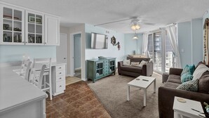 Een woonkamer met een bank, een salontafel, een televisie en een eethoek met stoelen en een tafel.