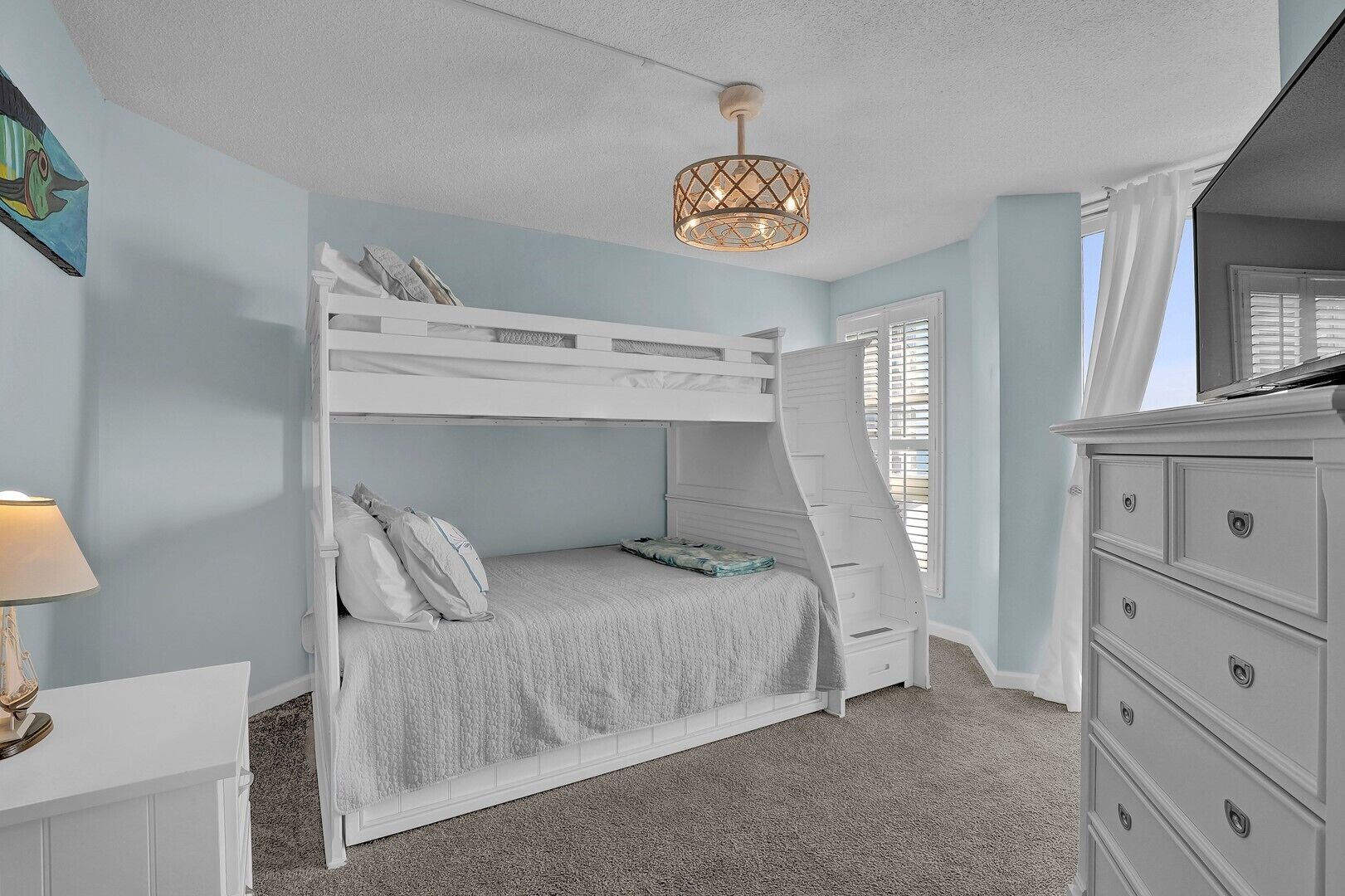 A bunk bed room with a ceiling light fixture, a dresser, and a window with blinds.