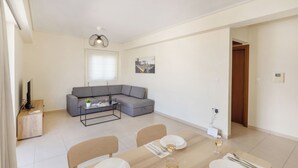 Una sala moderna con un sofá gris, una mesa de comedor para dos personas y una pequeña mesa de centro.