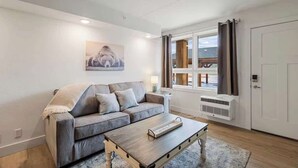 Un salon moderne avec un canapé gris, une table basse en bois et une grande fenêtre agrémentée de rideaux.