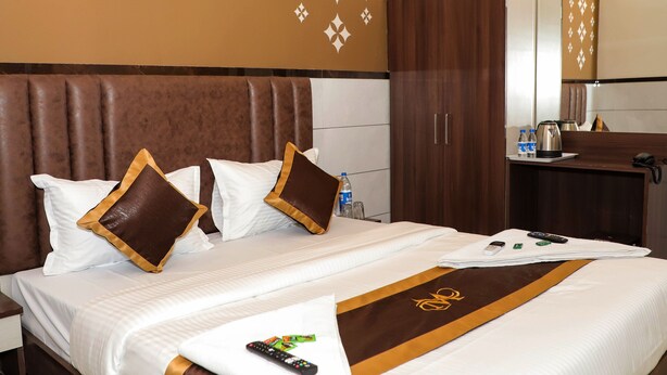 A hotel room with a large bed, a wooden headboard, a wardrobe, a bathroom with a mirror, and a small table with toiletries. - MAJESTIC INN (Vasai)